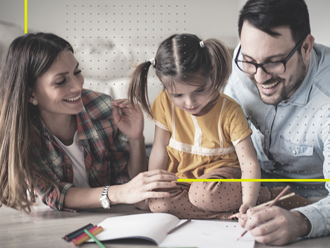 Una joven pareja, hombre, mujer, educando a su hija. Le están enseñando a dibujar. Todos están alegres.