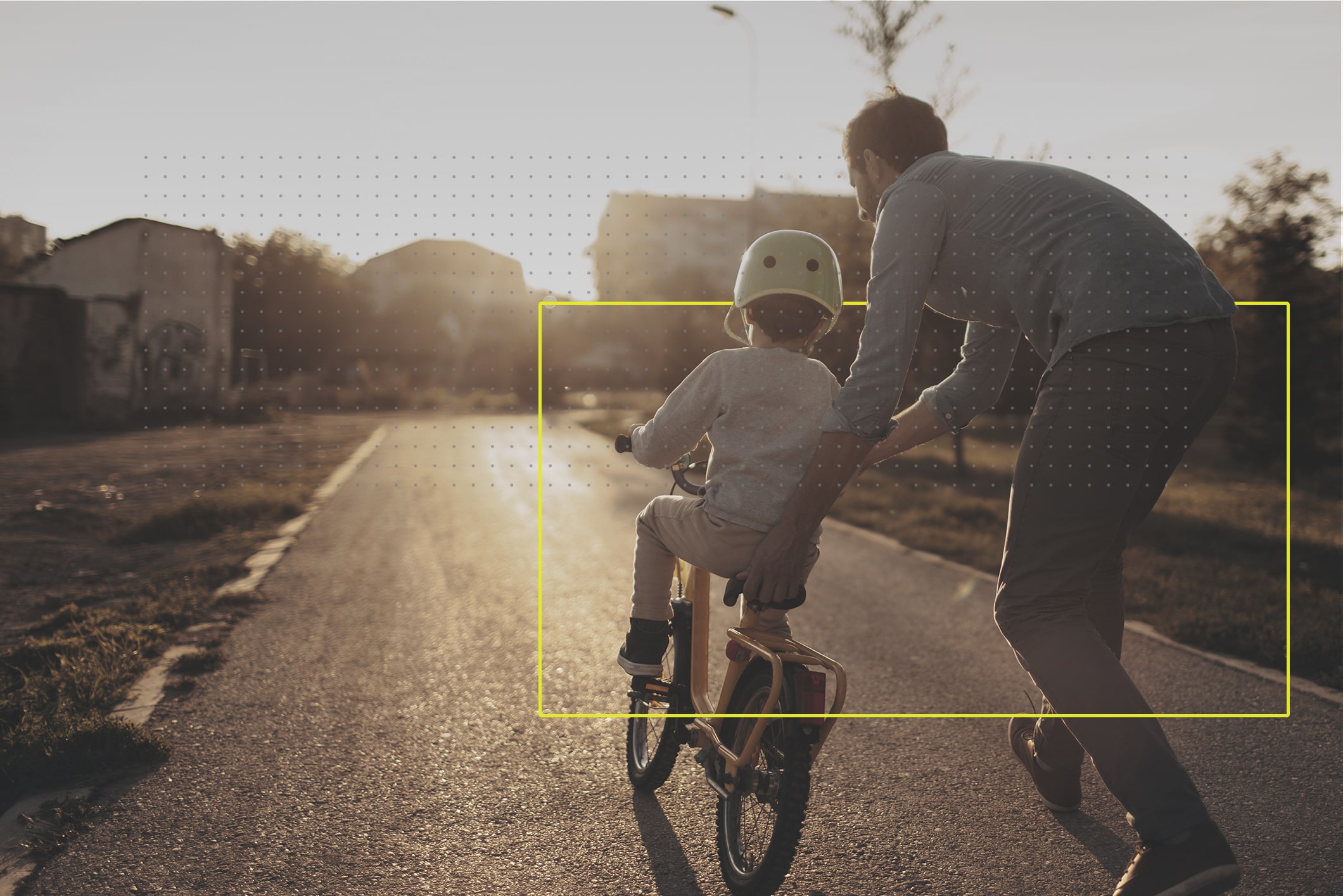 Dos personas, un hombre de mediana edad y un niño de 5 años aproximadamente, padre e hijo. Están en una calle. El padre le está enseñando a andar en bicicleta. 