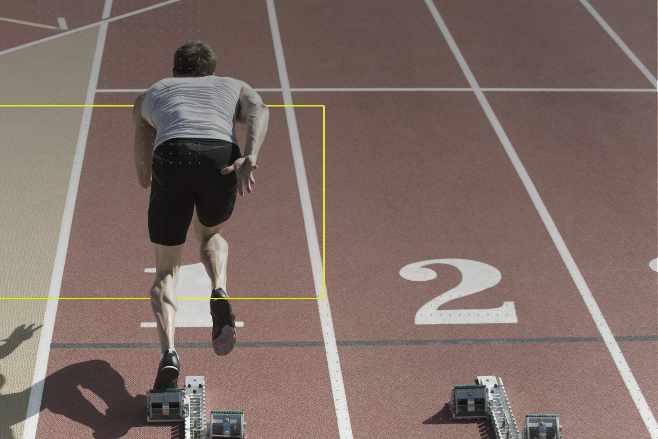 Una persona, hombre, en la lína de salida de una pista de atletisto que se prepara para comenzar la carrera.