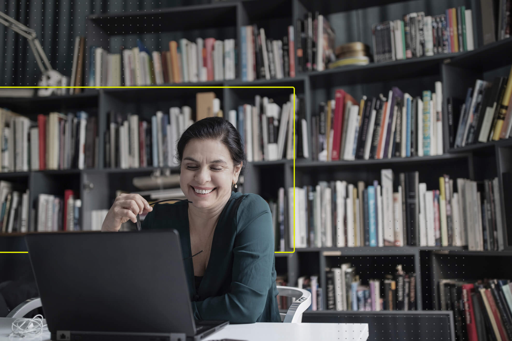 En primer plano se muestra una mujer mayor de negocios viendo su computadora. Está trabajando en su oficina con una bilblioteca de fondo.